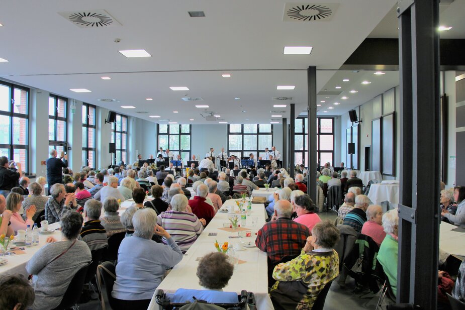 Ein Bild welches mehrere Menschen in einem Saal zeigt, welche den Klängen des sächsischen Polizeiorchesters lauschen. Dies ist im Stadtsaal Flöha. 